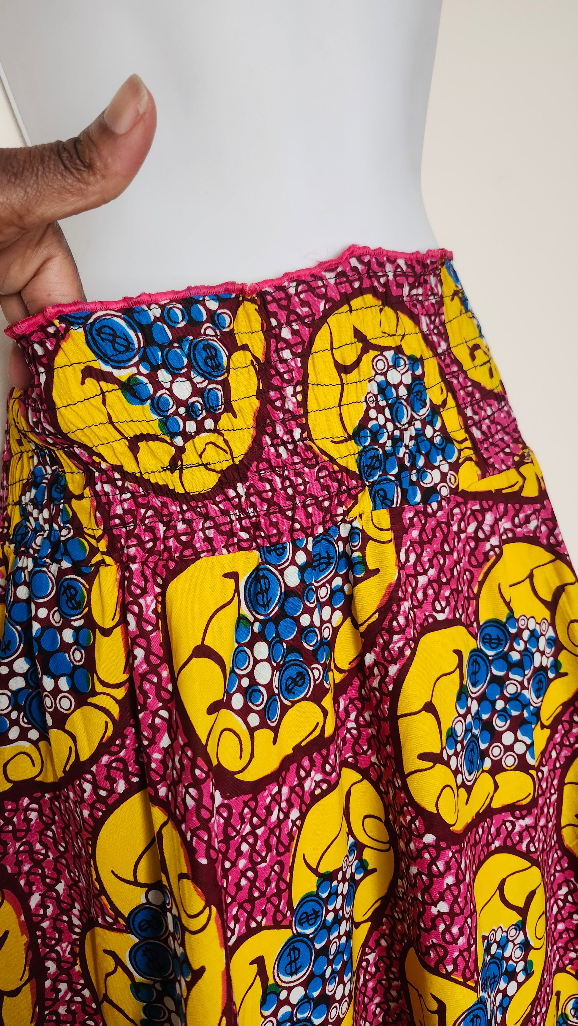 Hand holding a piece of colorful fabric with yellow and blue patterns on a white background