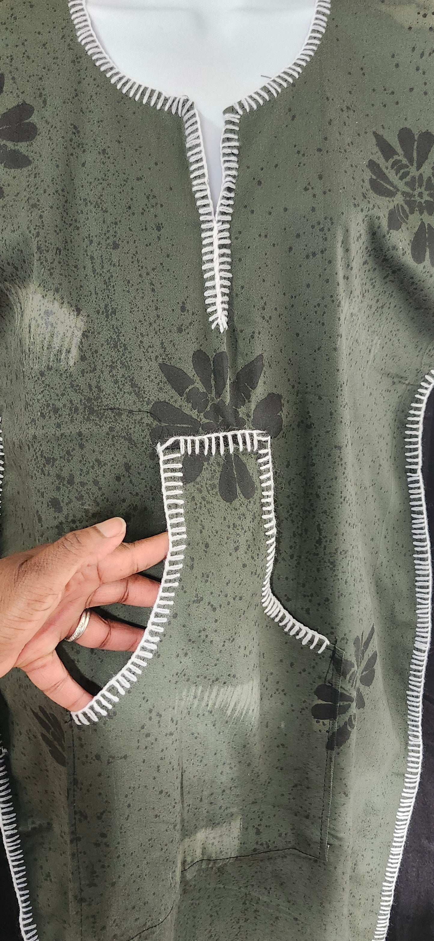 Hand holding a piece of fabric with floral embroidery on a green floral patterned dress showing pockets
