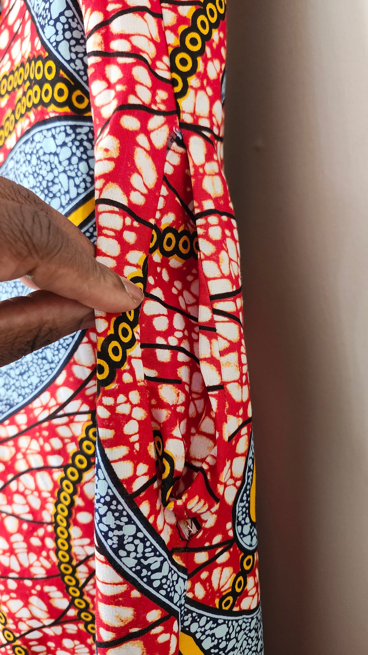 Person holding a piece of colorful fabric with intricate patterns on a plain background